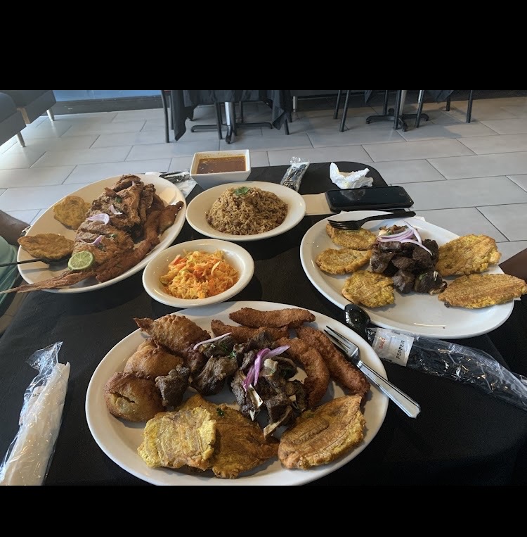 Table spread of Haitian dishes at Klas La, including griot, tassot, djon djon rice, and pikliz